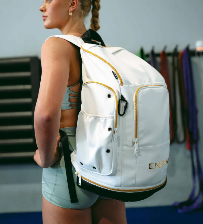 Woman wearing a white backpack with gold accents and gold 'Engine' branding