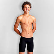 A young boy standing and smiling, wearing Funky Trunks black training jammers.