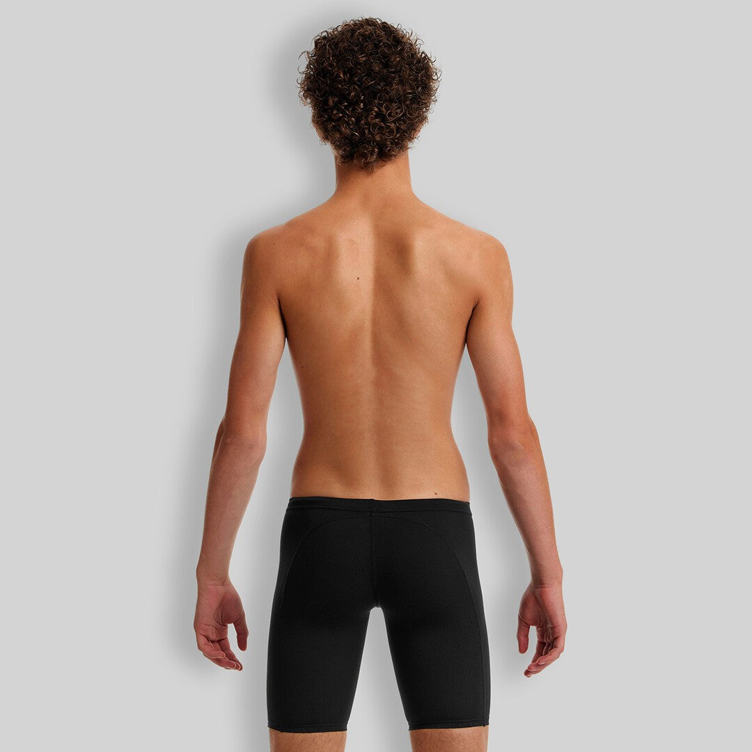 A young boy standing and smiling, wearing Funky Trunks black training jammers.