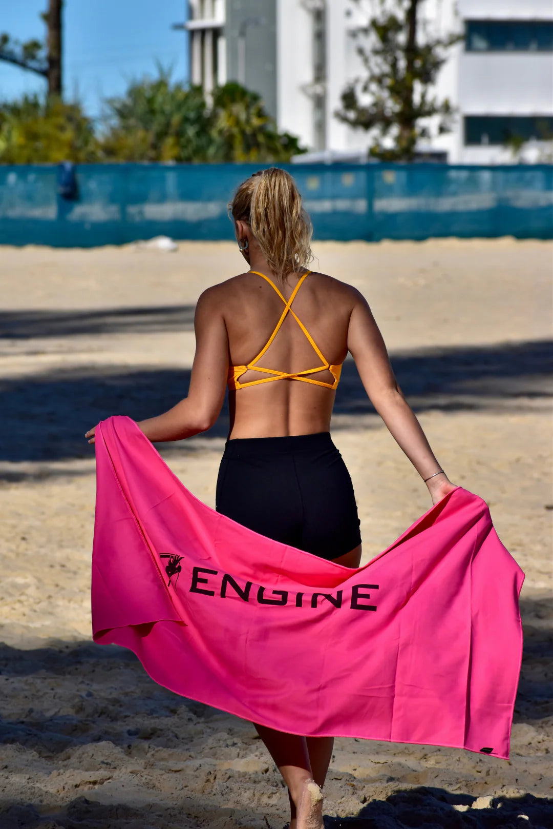 Woman on a beach holding a pink towel with 'Engine' branding