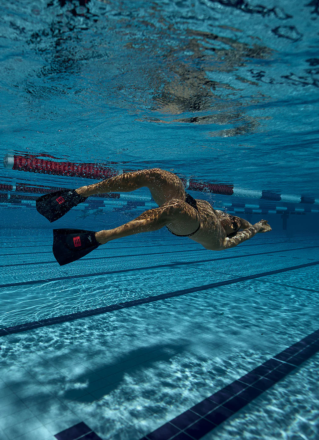 Photo of a swimmer on his back underwater wearing dmc elite max fins in anthracite black/red color.