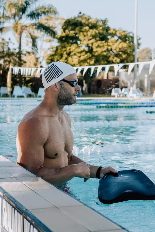 A male swimmer using a black Engine Elite kickboard in a pool.