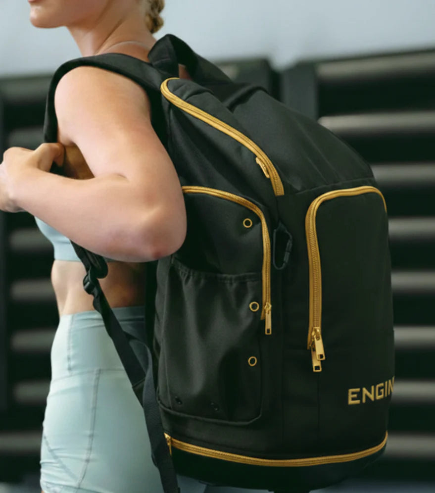 Woman wearing a black backpack with gold accents and gold 'Engine' branding