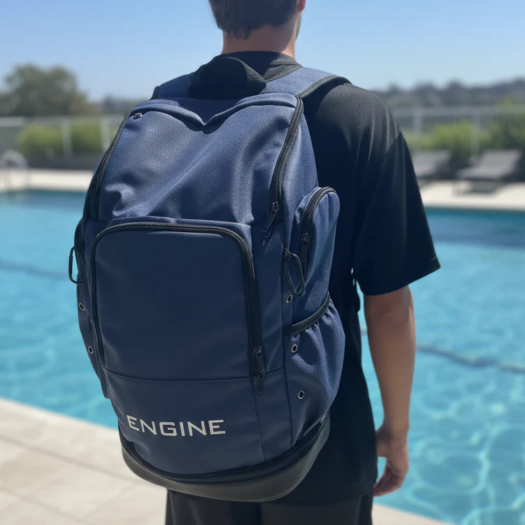 Back view of a man wearing a navy blue backpack with 'ENGINE' branding by a pool.