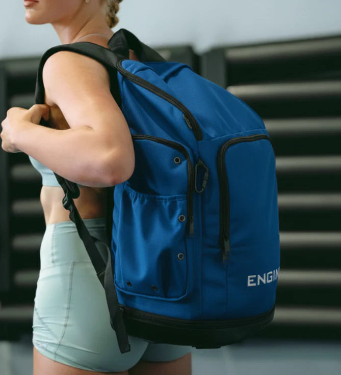 Side view of a woman wearing a royal blue backpack with 'ENGINE' branding in an indoor setting.