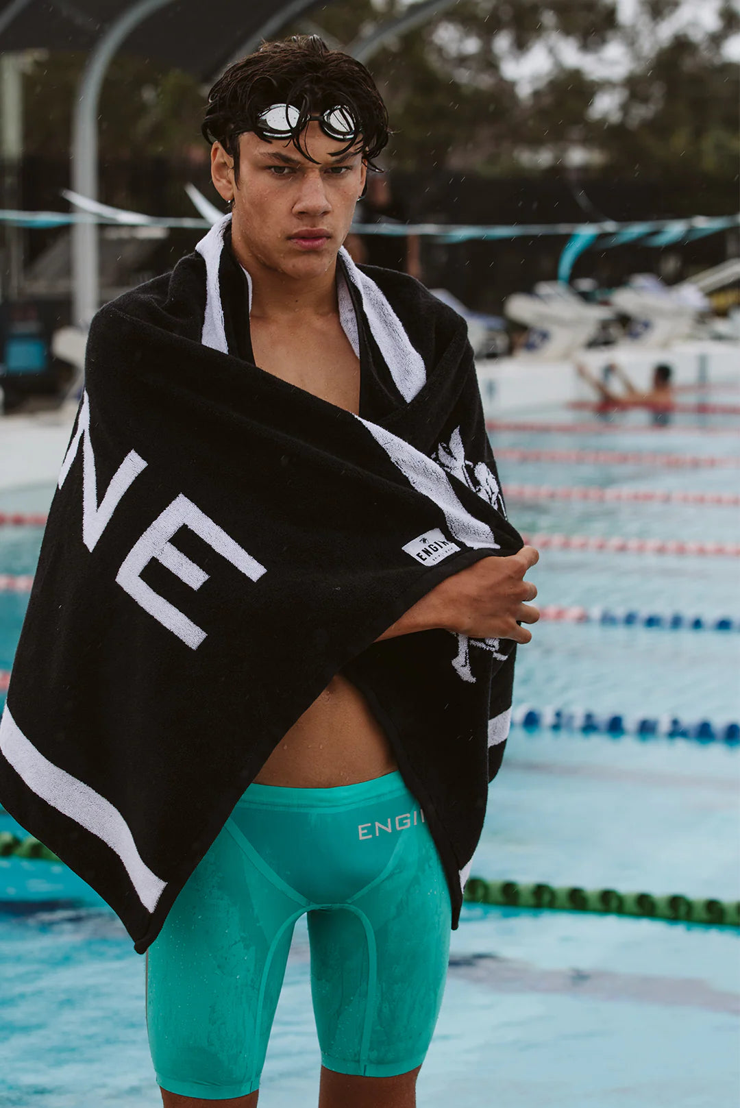 Male wrapped in a black towel with 'Engine' branding at a poolside.