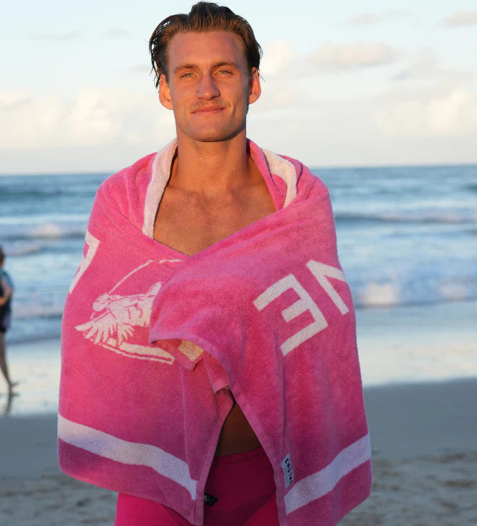 Man wrapped in a pink towel with the 'Engine' logo on a beach