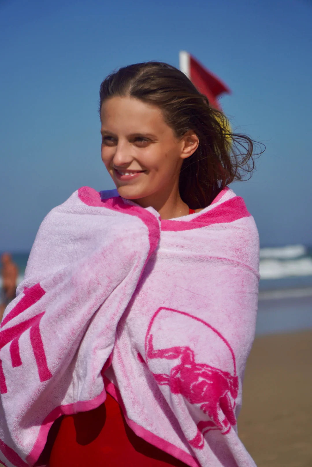 Woman wrapped in a pink towel with the 'Engine' logo on a beach