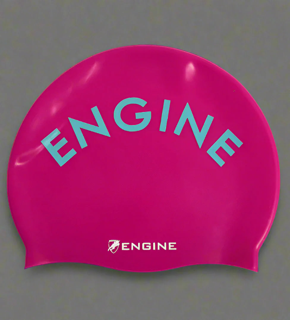 A raspberry pink swim cap with 'ENGINE' branding in turqua on a grey background