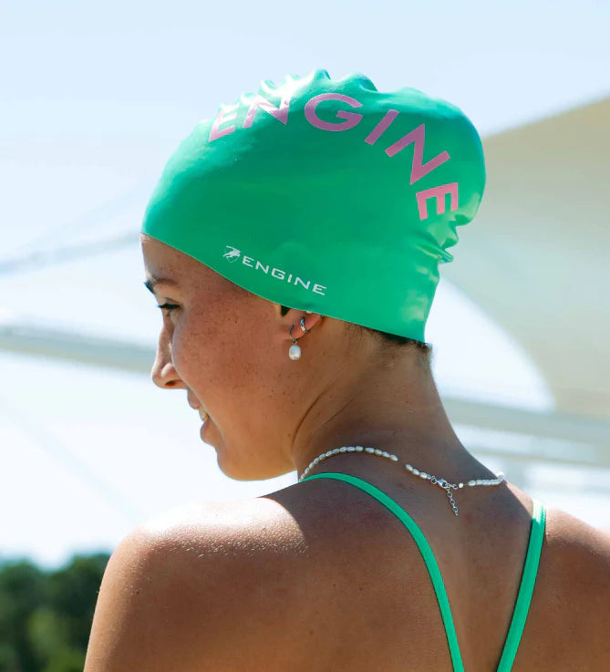 Woman wearing a green swim cap with 'ENGINE' branding in pink.