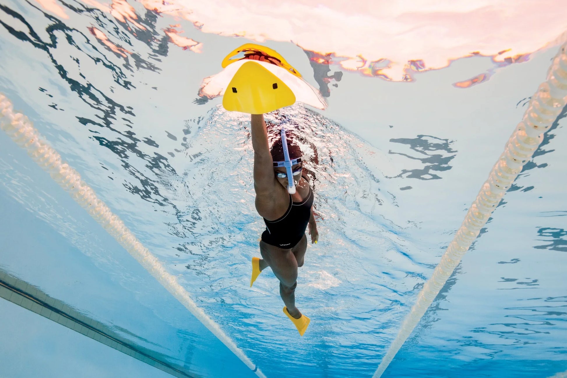 Person swimming underwater with a FINIS yellow alignment kickboard in a pool.