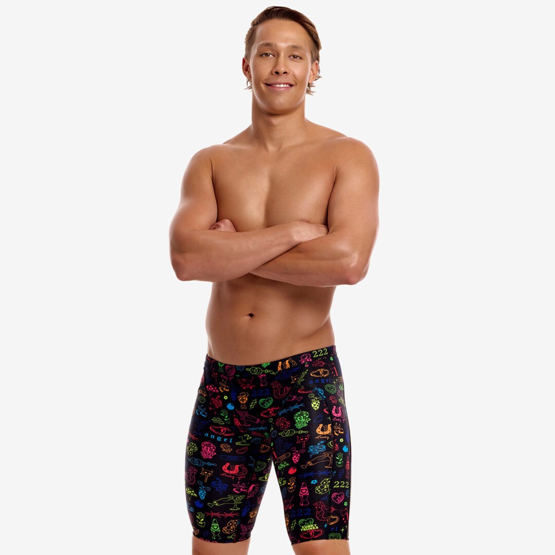 A shirtless male model with his arms crossed wearing multicoloured swimming jammers with a colourful "doodles" pattern from Funky Trunks 