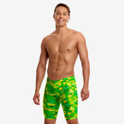 A shirtless male model wearing bright green and yellow geometric patterned pair of swimming jammers from Funky Trunks.