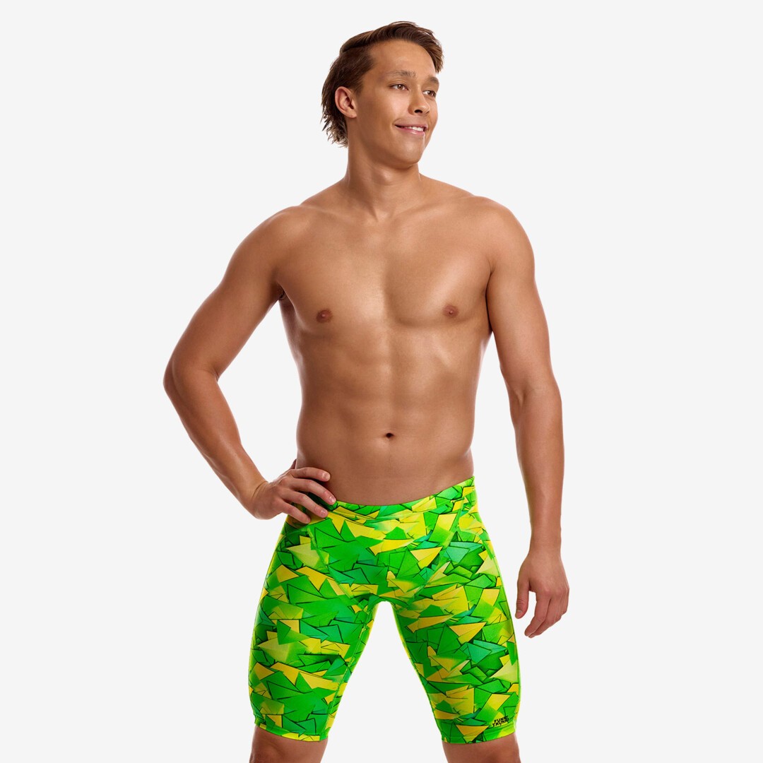A shirtless male model looking sideways wearing bright green and yellow geometric patterned pair of swimming jammers from Funky Trunks.