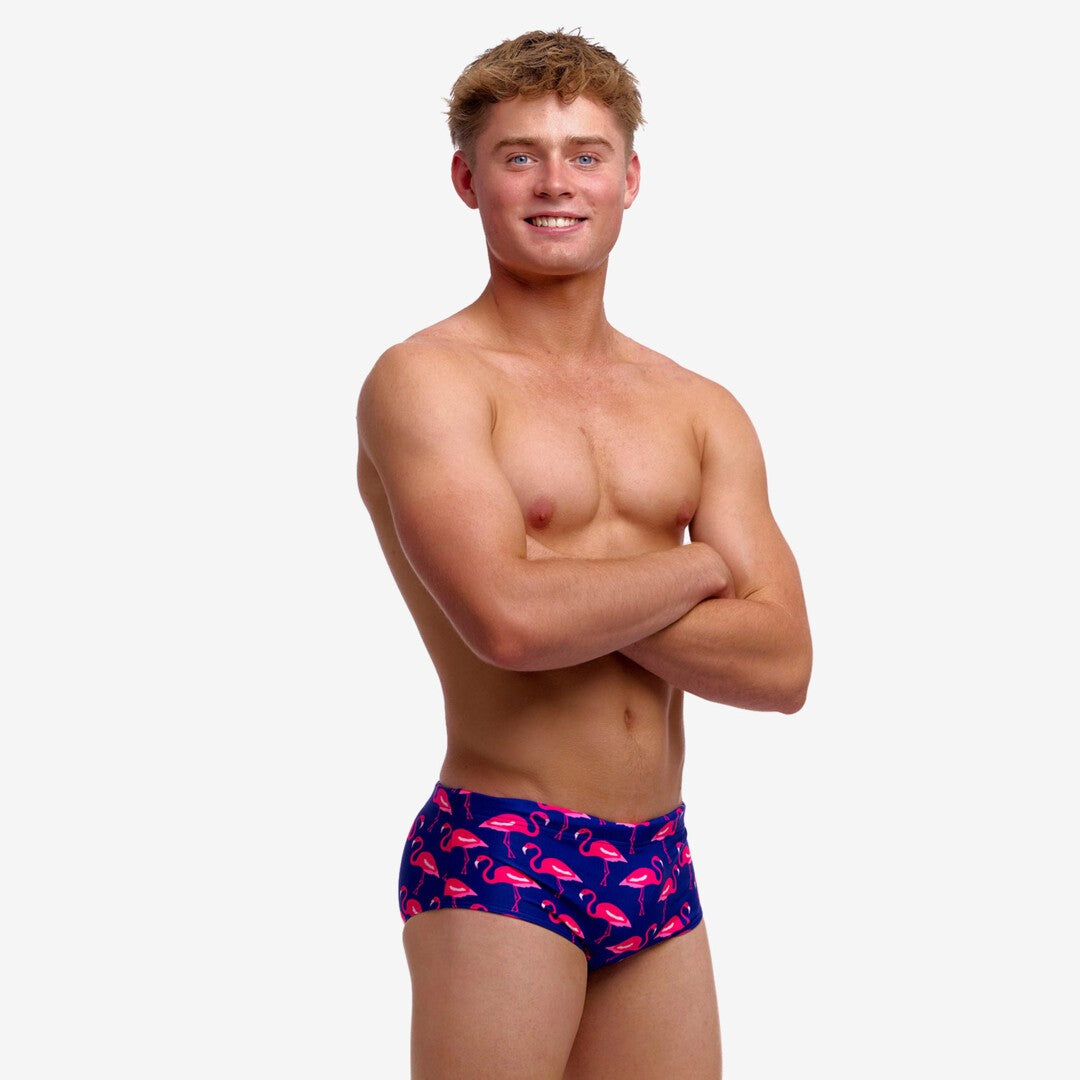 Boy wearing blue swim trunks with pink flamingo pattern on a white background