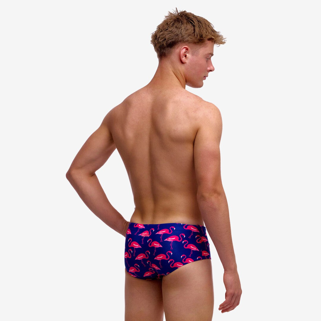 Boy wearing blue swim trunks with pink flamingo pattern on a white background