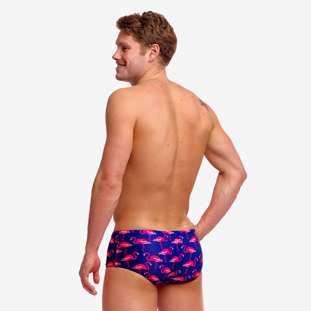 Back view of a man wearing a blue swim trunks with pink flamingo pattern on a white background