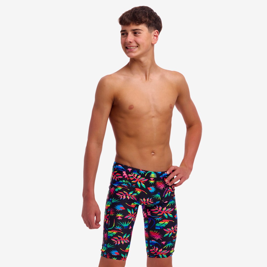 Young boy wearing colourful tropical leaf patterned swim jammers on a white background