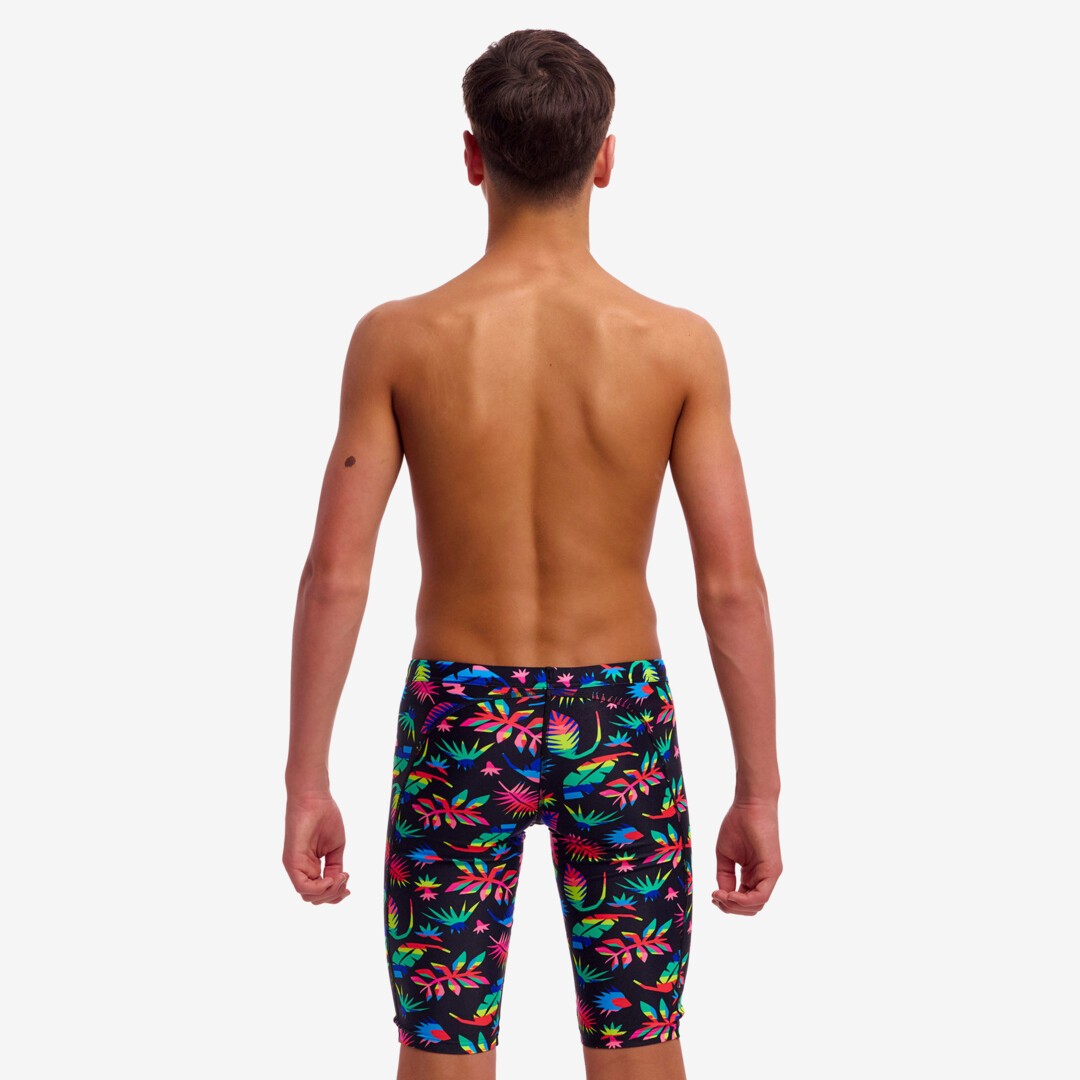 Back view of a young boy wearing colourful tropical leaf patterned swim jammers on a white background