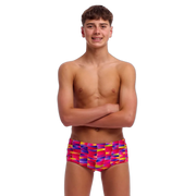 Boy wearing pink, purple and yellow colourful swim trunks on a white background