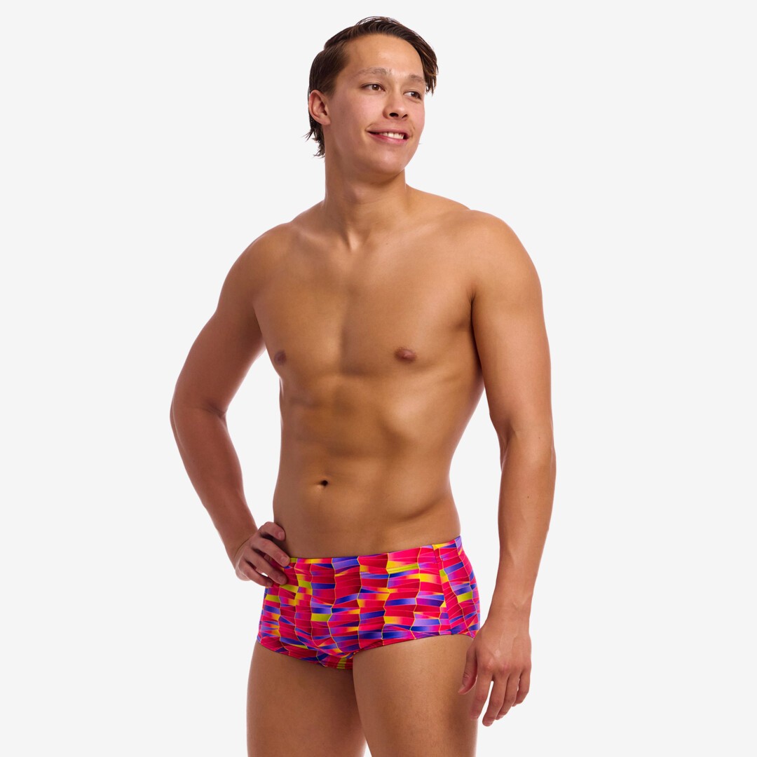 Man wearing colourful pink, purple and yellow swim trunks on a white background