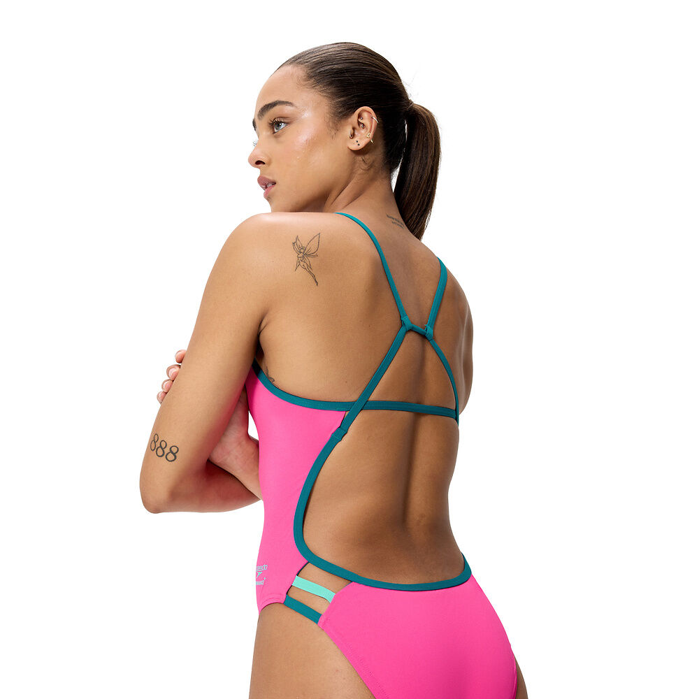 Side view of a woman wearing a 'SPEEDO' pink swimsuit showing teal strap details on a white background