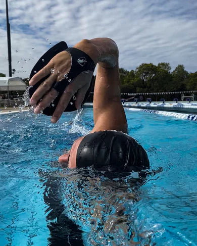 Person swimming in an outside pool wearing Engine black hand paddles