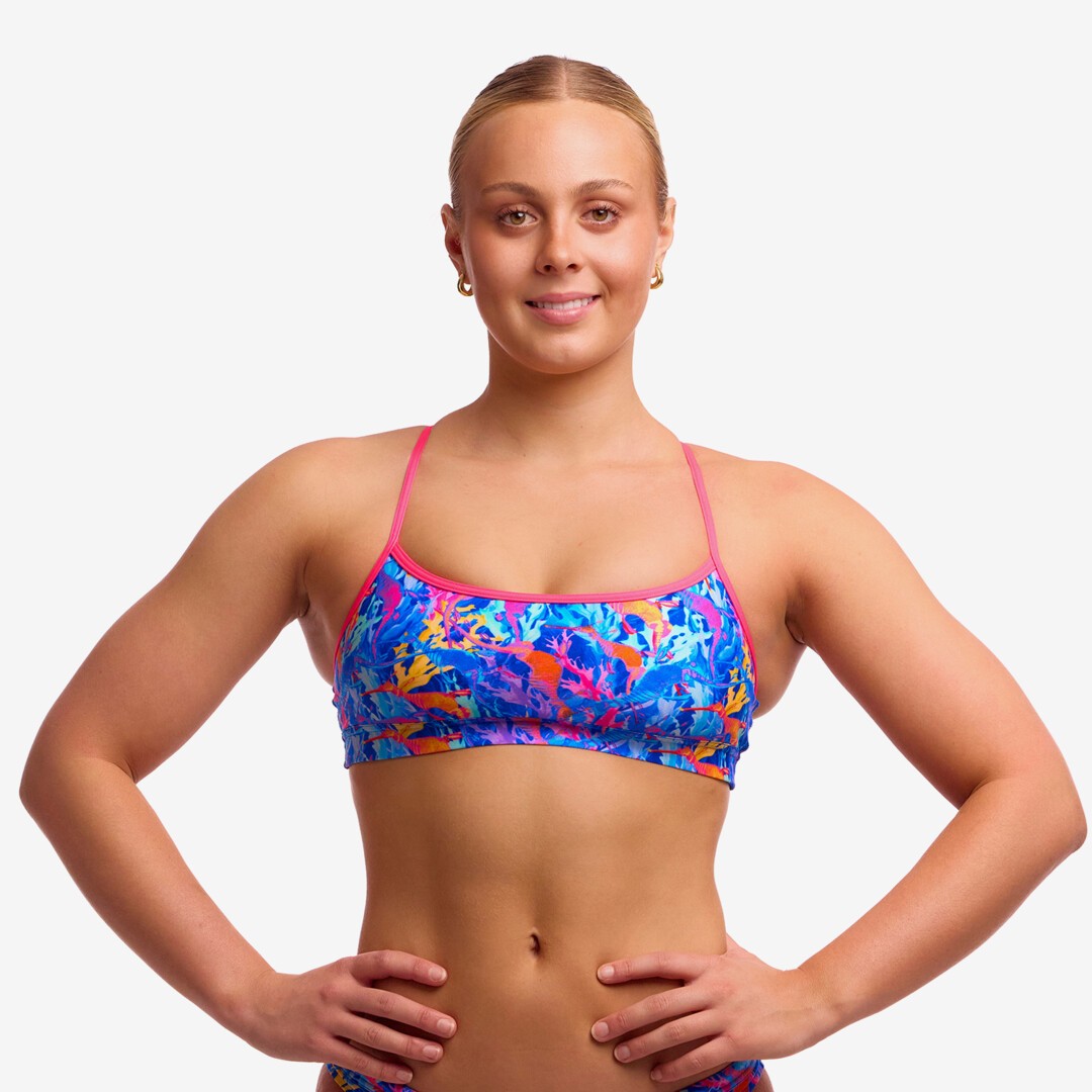 Woman wearing a colourful swim crop top top with pink coloured straps against a plain background