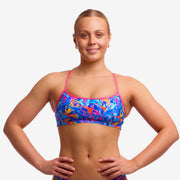 Woman wearing a colourful swim crop top top with pink coloured straps against a plain background