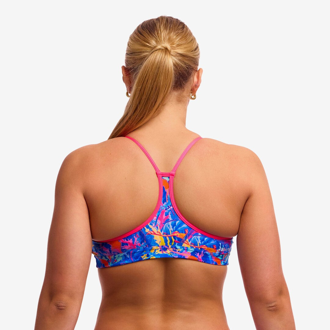 Back view of a woman wearing a colourful swim crop top top with pink coloured straps against a plain background