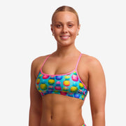 Woman wearing a colourful patterned swimming crop top with light pink straps on a plain background