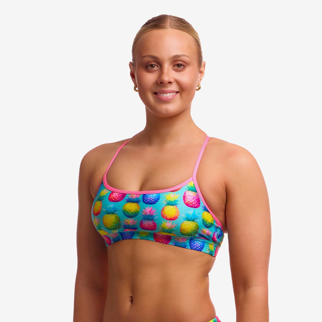 Woman wearing a colourful patterned swimming crop top with light pink straps on a plain background