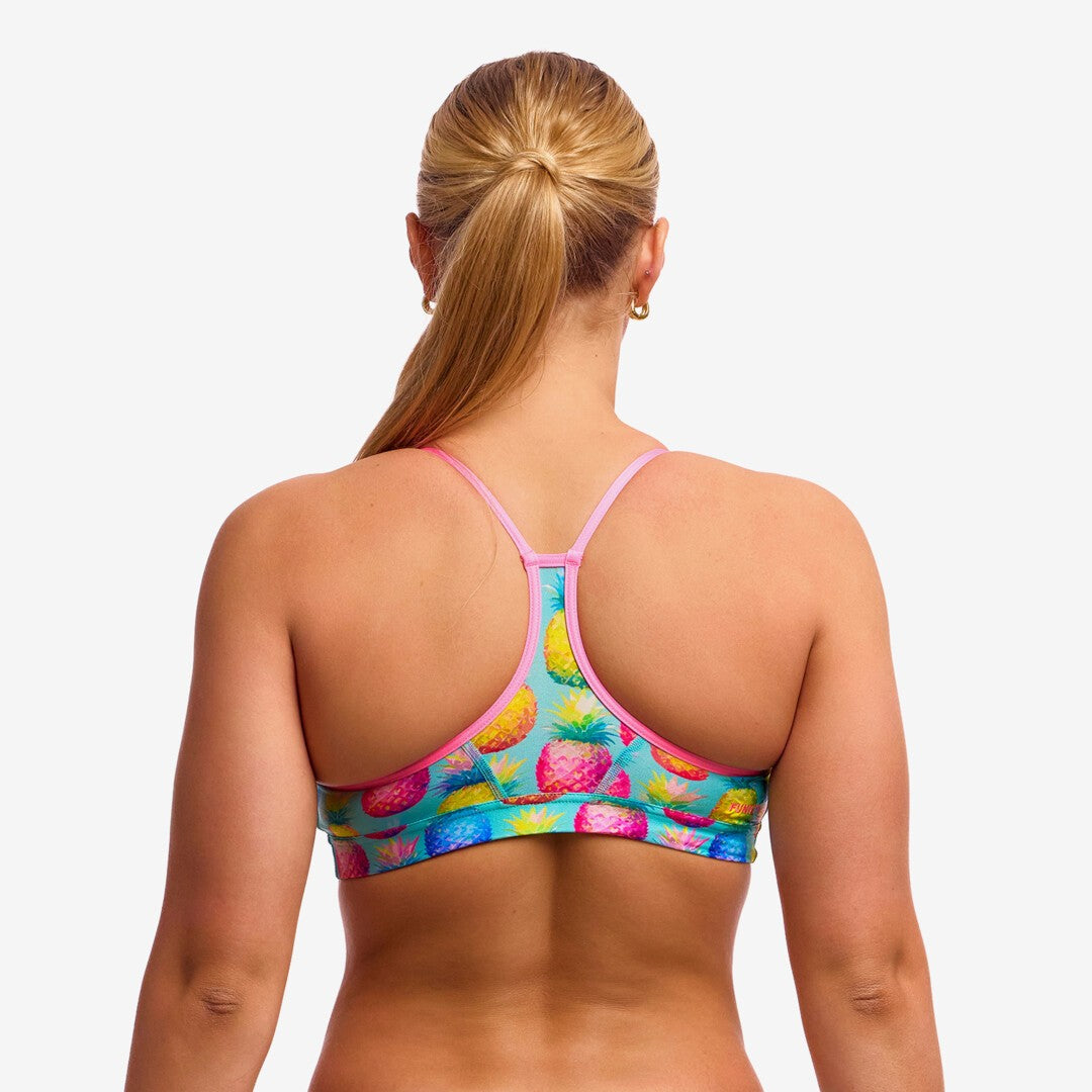 Back view of a woman wearing a colourful swim crop top with light pink straps on a white background