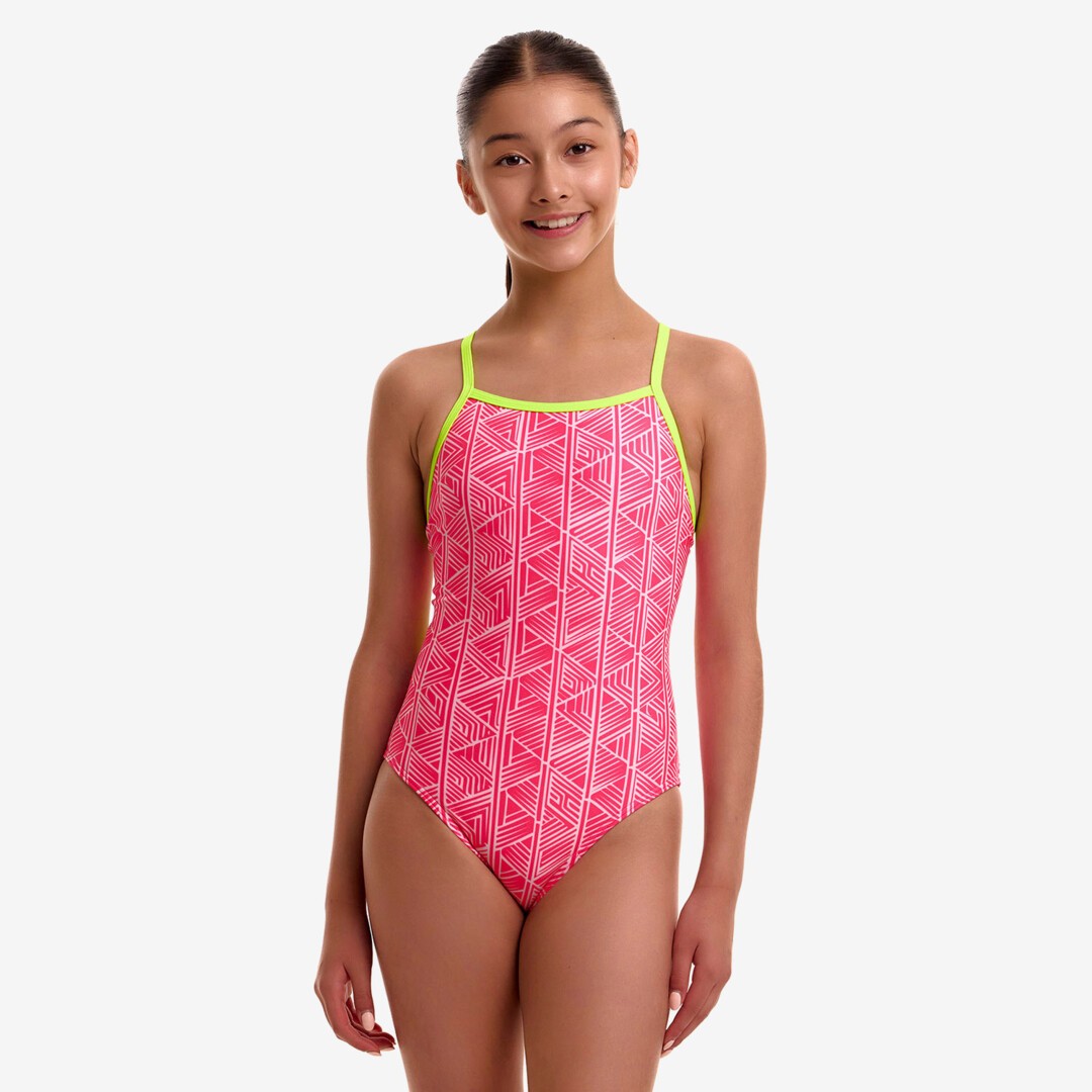 A young girl modeling a bright pink and white geometric patterned one-piece swimsuit with neon yellow straps, from the brand Funkita.