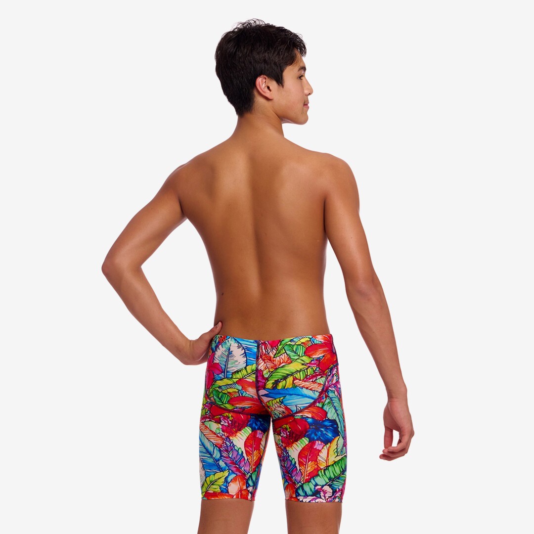 A young man shown from the back wearing colourful swim jammers with a tropical leaf pattern, against a white studio background.