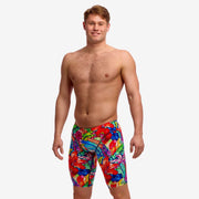 A male model wearing vibrant, multicolored swim jammers with a bold abstract pattern, standing against a white studio background.