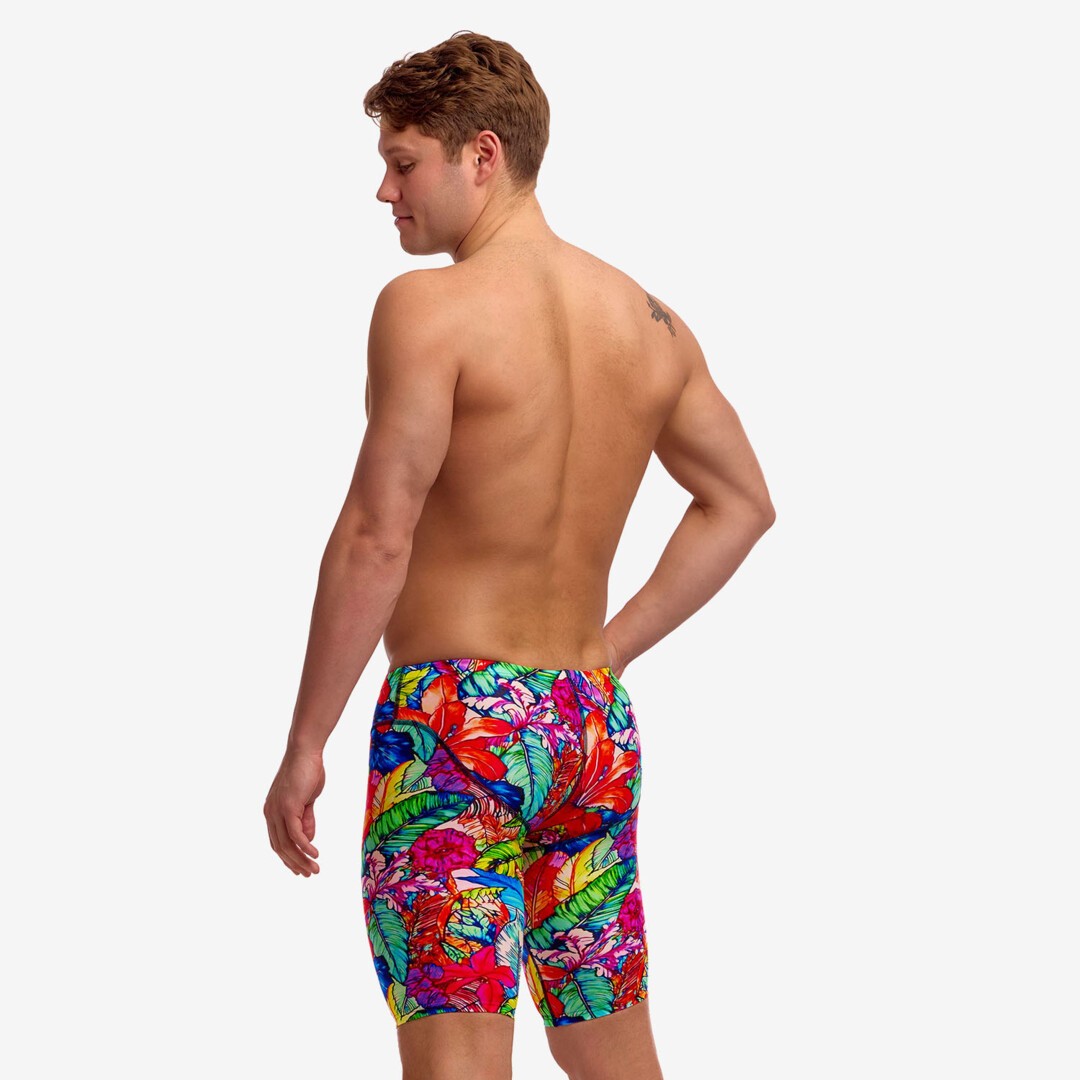 A man shown from the back wearing colourful tropical leaf print swim jammers against a white studio background.