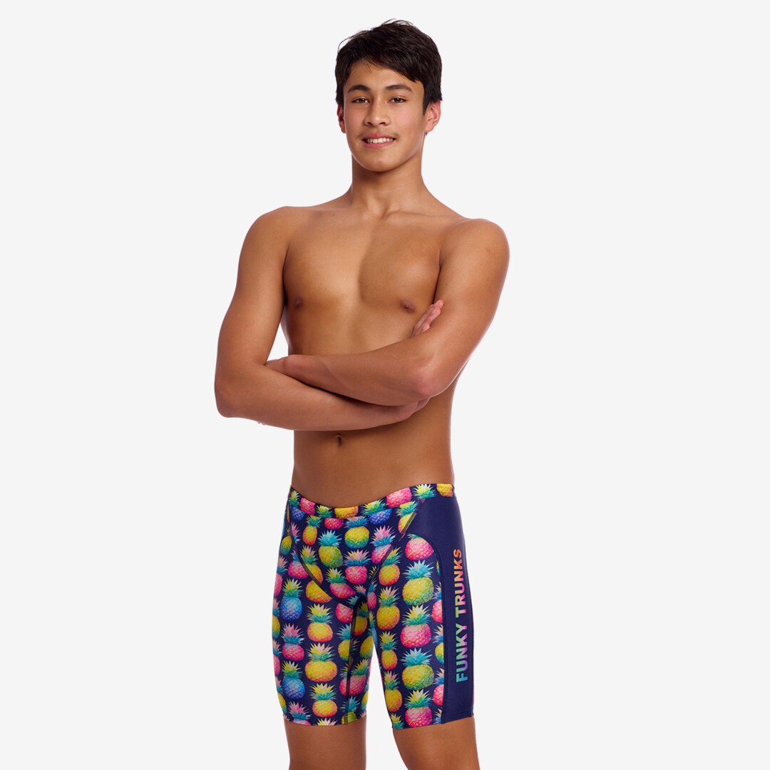 Boy wearing colourful pineapple-patterned swim jammers on a white background