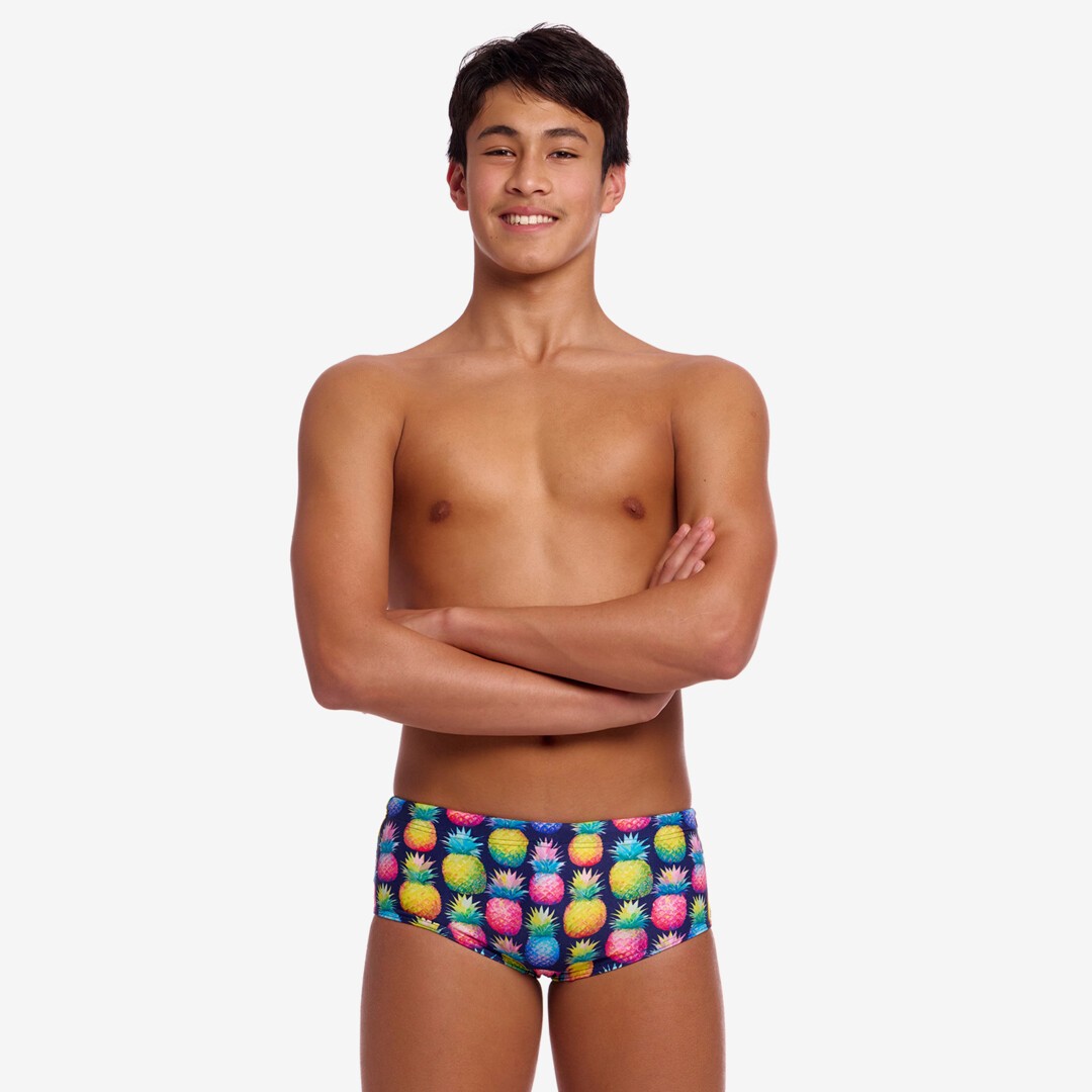 Boy wearing colourful pineapple-patterned swim briefs on a white background