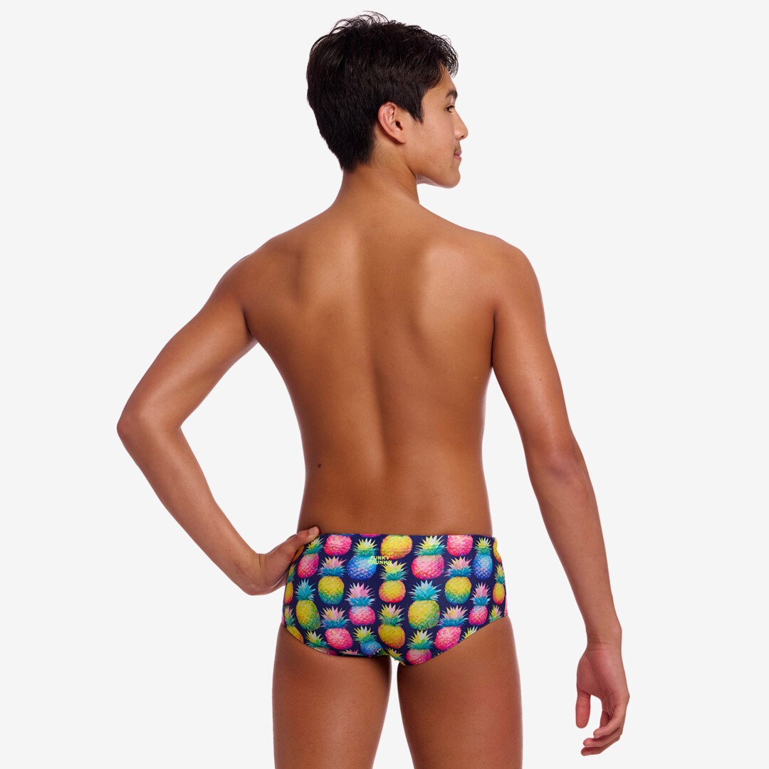 Back view of a boy colourful pineapple-patterned swim briefs on a plain background