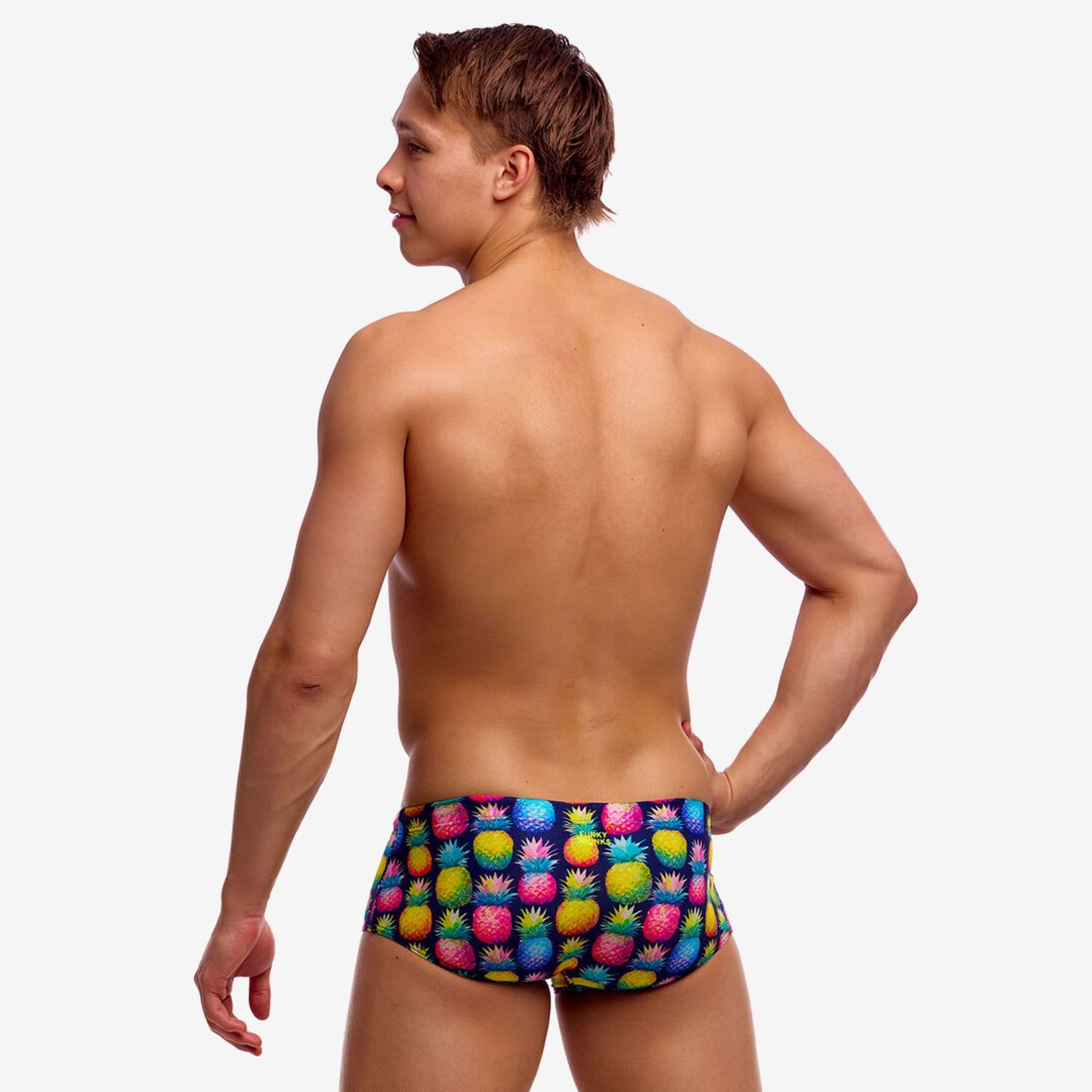 Back view of a man wearing colourful swim trunks with a pineapple pattern on a plain background