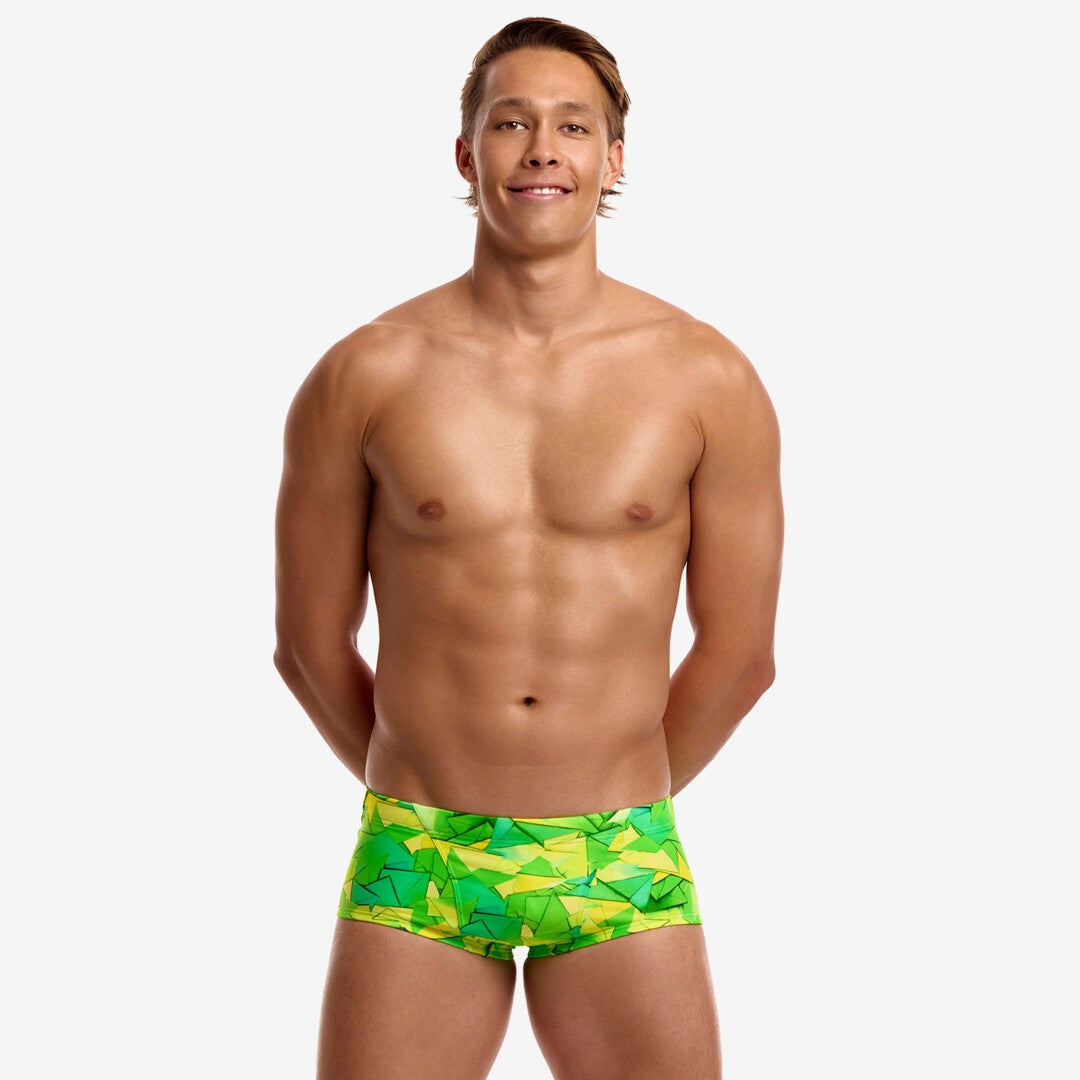 A shirtless man with arms behind the back wearing bright green and yellow geometric print swim trunks